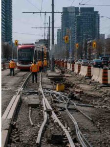 Construction crews repairing Finch West LRT tracks beside heavy Toronto traffic.