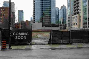 Empty Toronto construction site fenced off with a generic “Coming Soon” sign surrounded by condominium towers