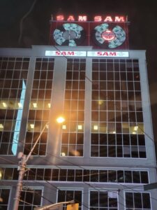 Restored Sam the Record Man neon spinning record signs lit at night above a modern Toronto building near Yonge-Dundas Square.