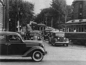 Black and white photo of downtown Toronto traffic in the 1930s with TTC streetcars and vintage automobiles crowding a city intersection.