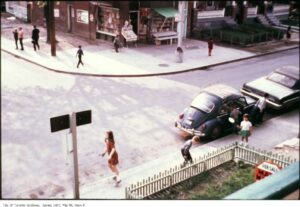 Vintage Toronto street scene showing a corner storefront, pedestrians, parked cars, and nearby houses, photographed from an elevated angle. City of Toronto Archives, Series 1465, File 98, Item 8.